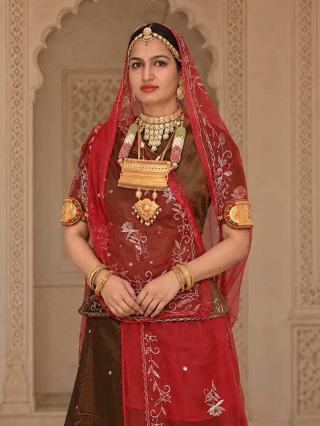 Brown kurti under a red odhni with silver vine borders and white flower motifs, draped over the head