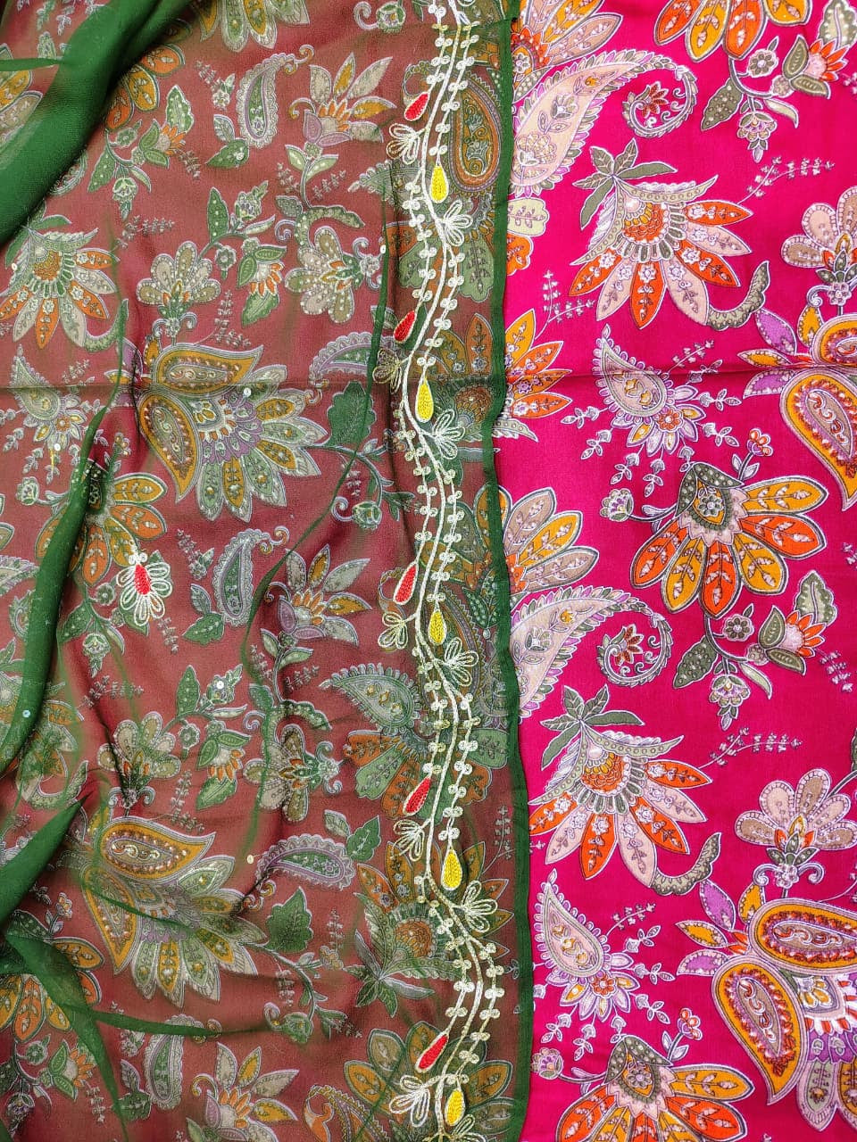Close-up of a fabric with pink and red floral patterns and green border.