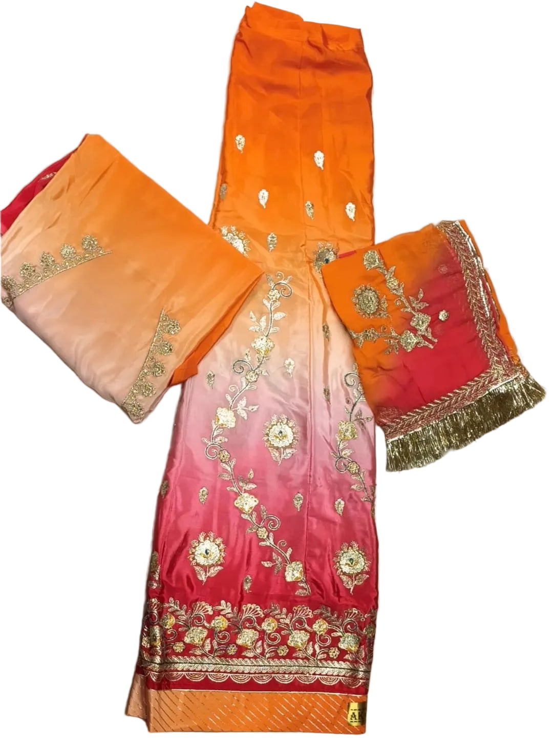 An embroidered traditional South Asian outfit laid flat on a wrinkled light gray fabric background. The garment features a vibrant color gradient transitioning from bright orange at the top, through peach and pink, to a rich magenta-pink at the bottom, adorned with intricate gold and silver floral embroidery and a decorative border.