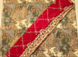 A close-up of a traditional embroidered fabric, likely a saree or textile, featuring a vibrant red border with intricate gold, beige, and white floral embroidery, set against a paisley patterned background of beige, gray, and gold.