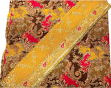 A close-up of a richly patterned fabric, likely a saree or textile, featuring a mustard yellow dupatta draped diagonally over a matching body fabric. The fabric has an intricate paisley and floral pattern in brown, bright pink, and gold zari embroidery.