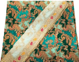 A close-up of a traditional patterned fabric, likely a saree or dupatta, featuring a teal green base with intricate gold, red, and orange paisley motifs and a wide white border with gold embroidery.