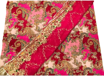 A folded textile with a rich magenta pink and light pink background, decorated with an intricate gold paisley and floral pattern, and a matching metallic gold border.