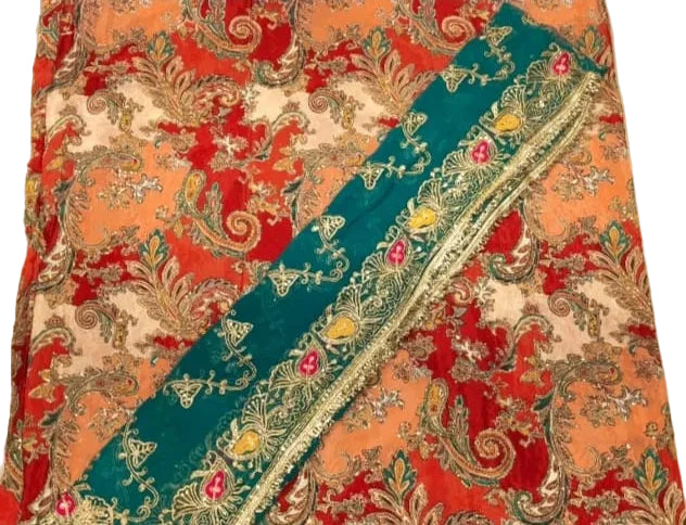 A close-up of a patterned textile, likely a sari or scarf, featuring a diagonal teal border with floral embroidery over a red, orange, and cream paisley background.