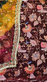 Close-up of an embroidered fabric with a dark brown base and dense floral motifs in pink, orange, blue, and gold, plus a decorative multicolor border.