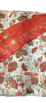 A close-up of a traditional embroidered fabric set, featuring a light blue base with a floral and vine pattern in rust red, gold, and green, accented by a solid rust red border with colorful floral embroidery.