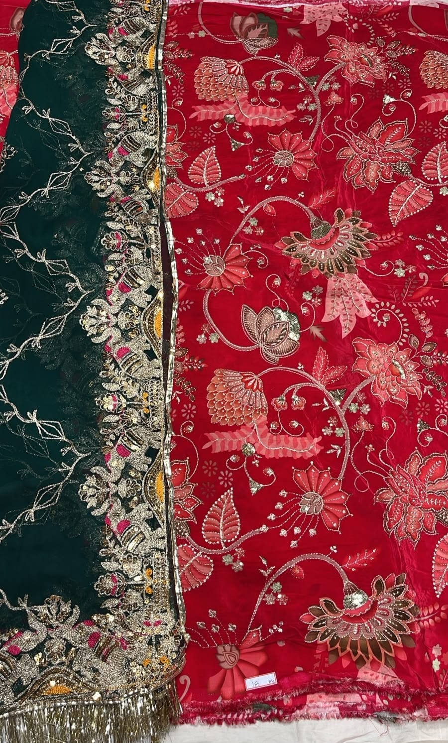 A close-up of a richly embroidered fabric, likely a dupatta or scarf, featuring a deep red side with pink and gold floral motifs and a dark green side with ornate gold embroidery and mirror work.