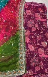 A folded traditional Indian salwar suit fabric set featuring a deep magenta floral printed body fabric and a bright green dupatta with pink and orange floral patterns and silver mirror work borders.