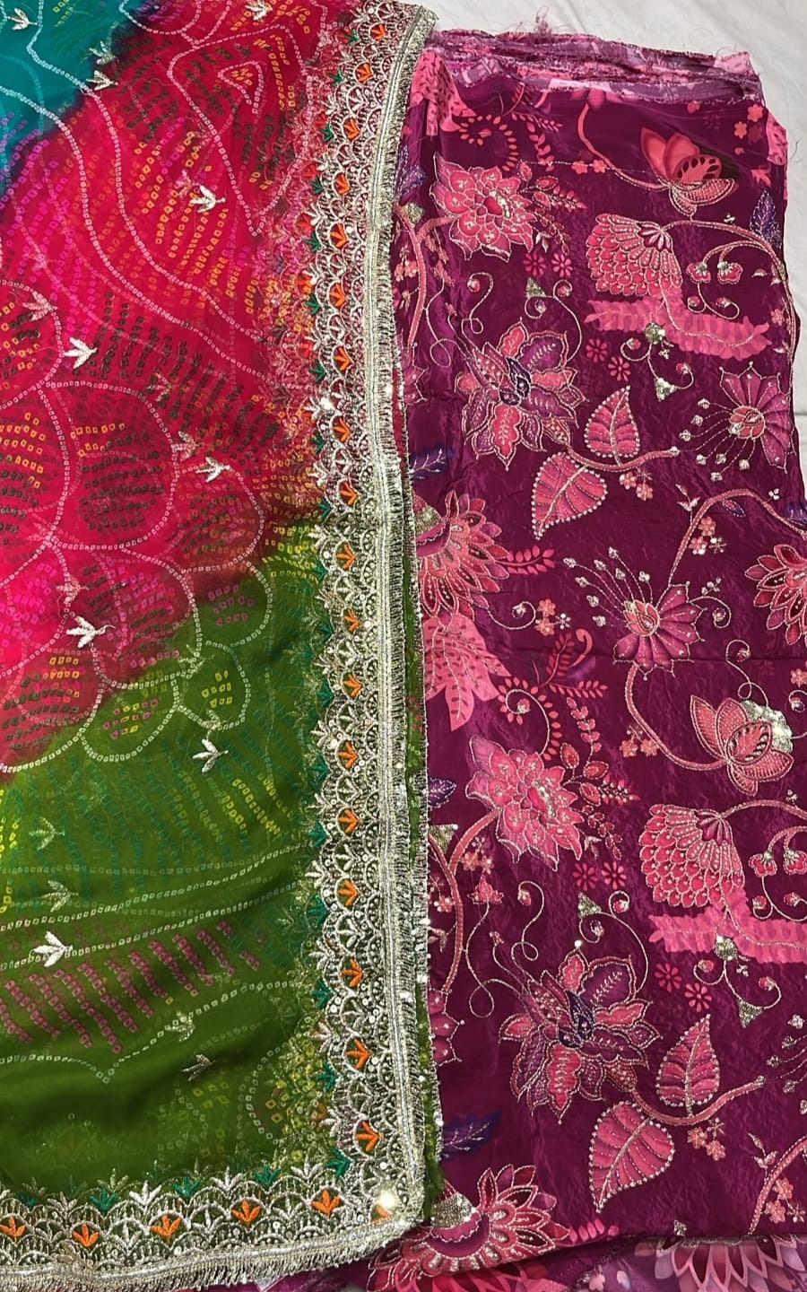 A folded traditional Indian salwar suit fabric set featuring a deep magenta floral printed body fabric and a bright green dupatta with pink and orange floral patterns and silver mirror work borders.