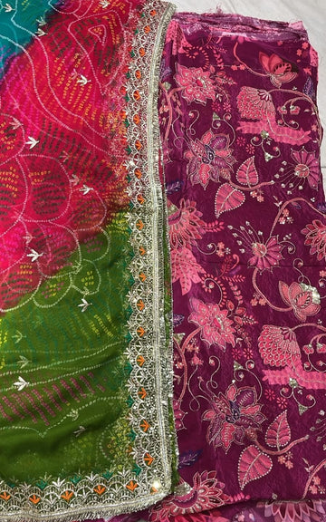 A folded traditional Indian salwar suit fabric set featuring a deep magenta floral printed body fabric and a bright green dupatta with pink and orange floral patterns and silver mirror work borders.