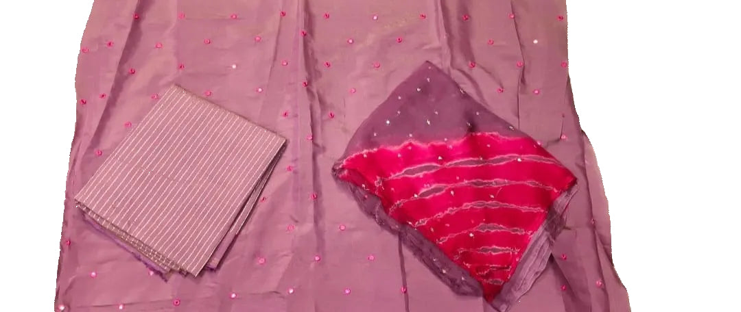 A folded pink and purple fabric set, likely a traditional dress material or saree fabric, laid out on a white sheet. One folded section shows a light pink striped fabric, while the other displays a sheer purple fabric with small pink dots and a vibrant pink dupatta featuring horizontal silver mirror work.
