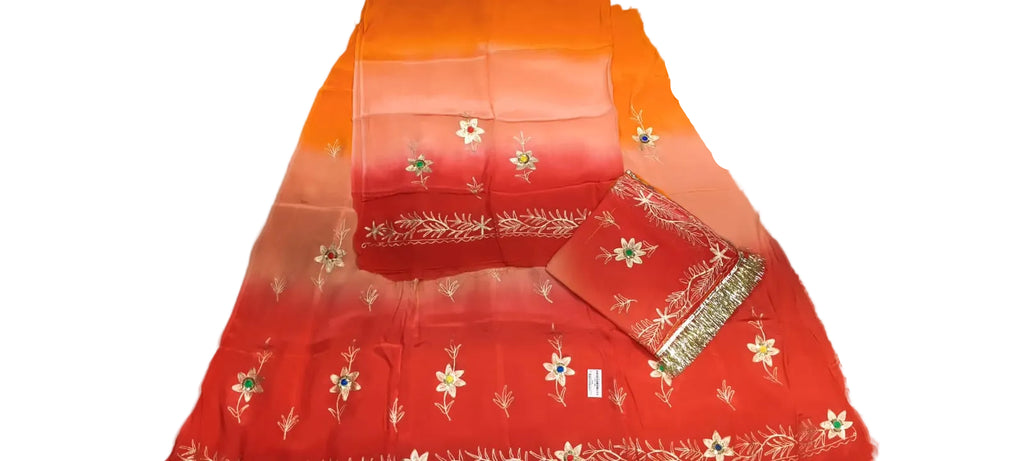 A folded red and orange gradient fabric set with white floral embroidery and gold zari borders, laid out on a white wrinkled surface.