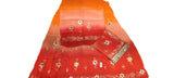 A folded red and orange gradient fabric set with white floral embroidery and gold zari borders, laid out on a white wrinkled surface.