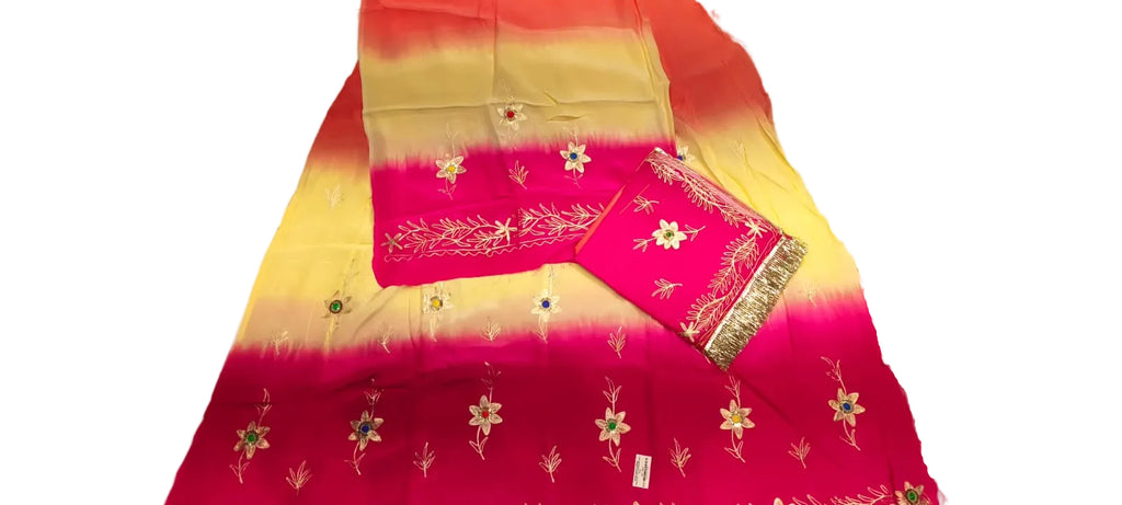 A folded bright pink and yellow gradient fabric with white floral embroidery and a patterned border, laid on a light-colored surface.