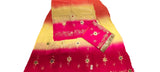 A folded bright pink and yellow gradient fabric with white floral embroidery and a patterned border, laid on a light-colored surface.