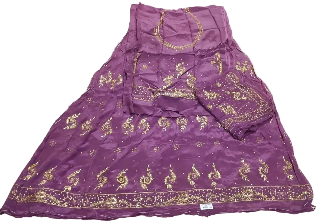 A purple traditional dress set with gold embroidery, laid flat on a wrinkled off-white sheet. The set includes a flared skirt, a matching sleeve, and a blouse piece with gold patterns.