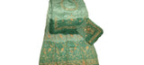 A green ethnic salwar suit set with gold embroidery laid out on a white fabric surface, including a kurta, matching pants, and a dupatta.