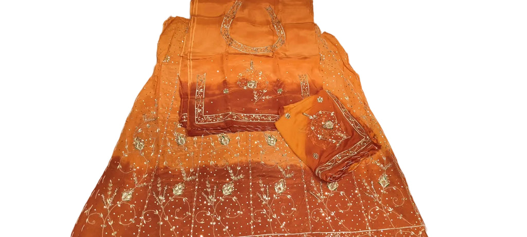 An orange and rust-colored traditional Indian salwar suit set laid out on a white sheet, featuring a kurta with silver mirror work, a matching bottom fabric, and a dupatta.