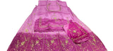 A folded magenta pink embroidered salwar suit set with gold metallic embroidery, displayed on a white floor next to a person's hands and legs.