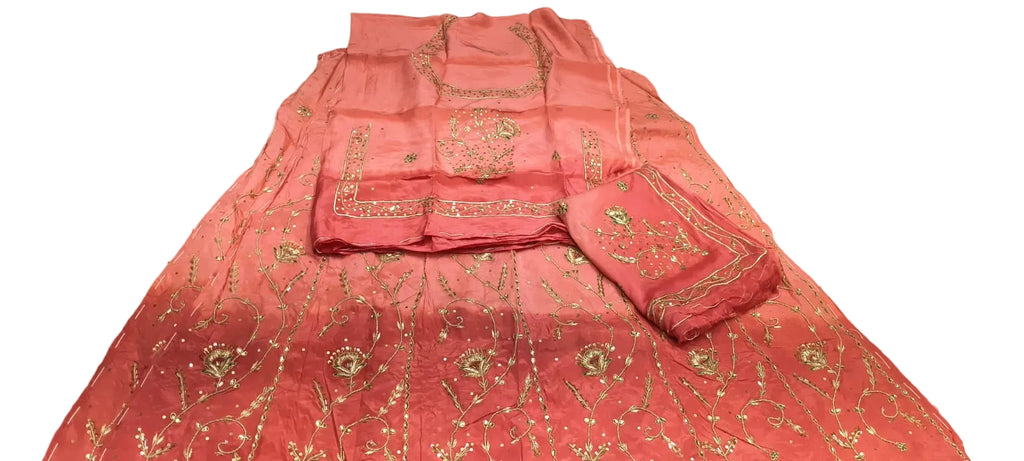 A pink embroidered traditional outfit laid flat on a white sheet, with matching dupatta and folded sleeves. The fabric has gold floral embroidery and metallic embellishments.