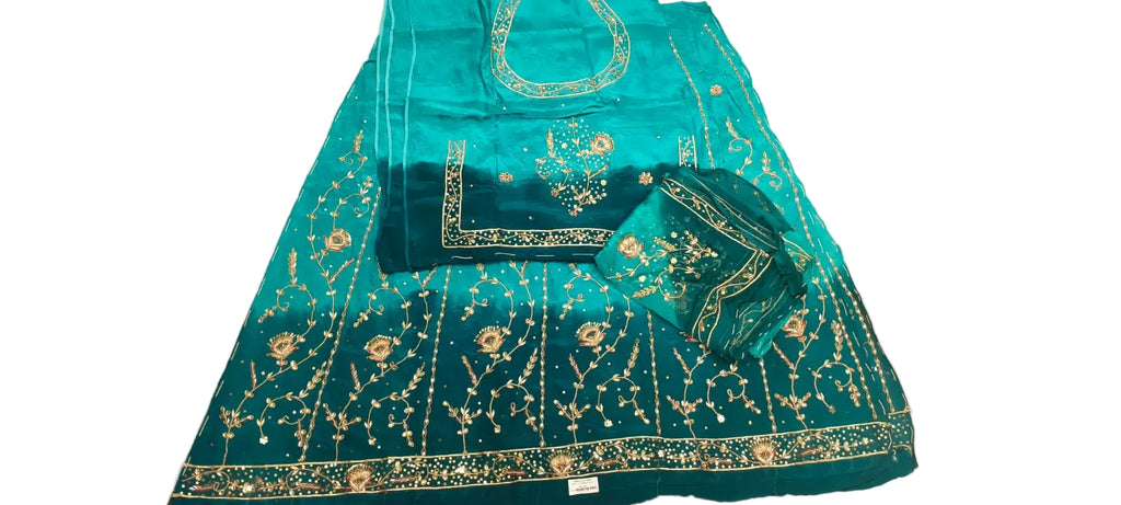 A teal blue and green embroidered ethnic suit set laid flat on a white fabric surface, featuring a kurta, dupatta, and matching embroidered fabric pieces with gold and silver embellishments.