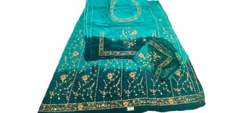 A teal blue and green embroidered ethnic suit set laid flat on a white fabric surface, featuring a kurta, dupatta, and matching embroidered fabric pieces with gold and silver embellishments.