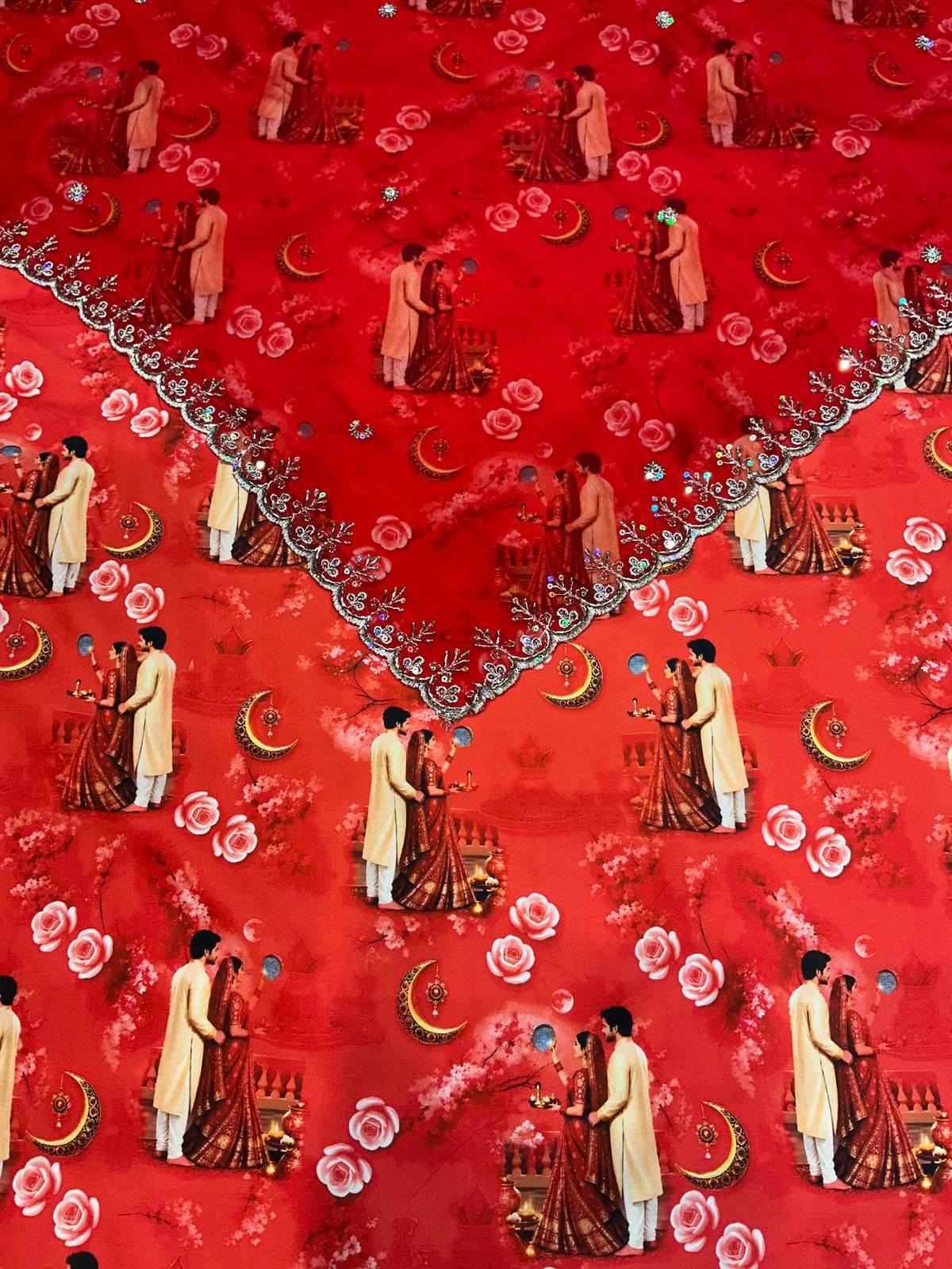 Close-up of Rajan cutwork odhni with a scalloped silver border and sequin flower vines, over red Karwa Chauth couple print fabric