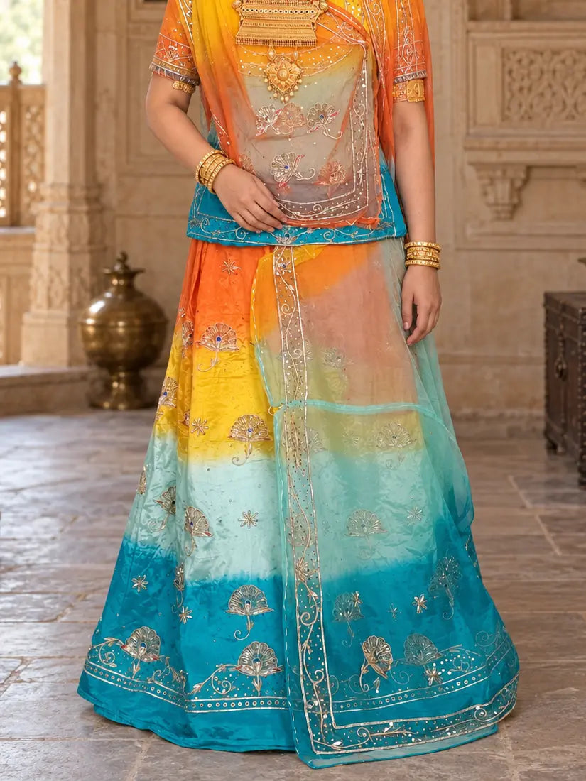 Lehenga close-up showing the orange-to-firozi shading, silver fan motifs with blue stones, and a wide silver hem border