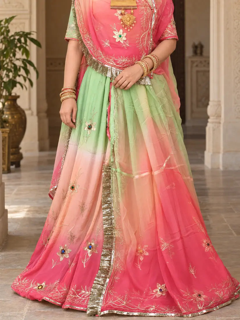 Lehenga flare in green, peach and pink, with scattered zari flowers set with blue, green and red stones, a zari vine hem border and the odhni fringe down the centre