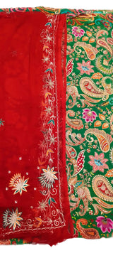 A traditional Indian ethnic garment, likely a saree or dupatta, featuring a vibrant red border with intricate gold, white, and green embroidery, and a green body adorned with colorful paisley and floral patterns.