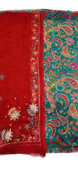A folded traditional fabric set, likely a salwar kameez or dupatta set, featuring a solid red side with white and gold floral embroidery and a teal paisley patterned side with red, gold, and pink embroidery.