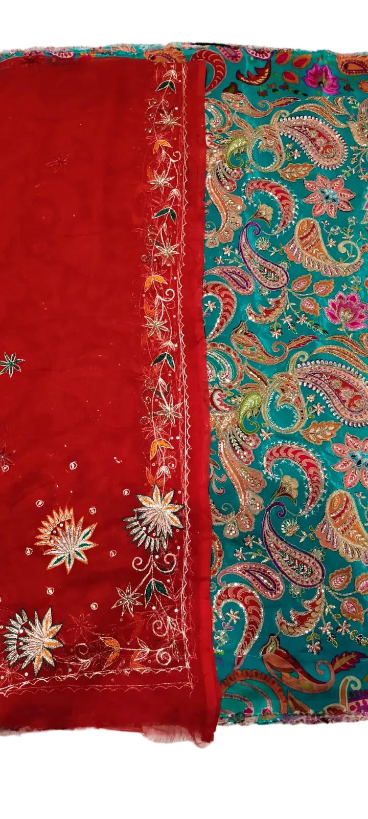 A folded traditional fabric set, likely a salwar kameez or dupatta set, featuring a solid red side with white and gold floral embroidery and a teal paisley patterned side with red, gold, and pink embroidery.