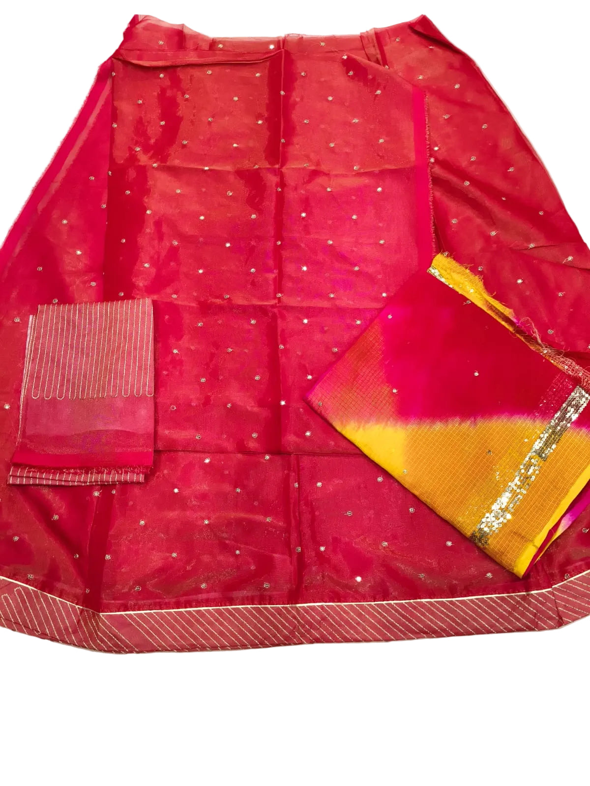 A folded red and pink fabric garment laid flat on a white sheet, with small metallic dot embellishments across the main body, a striped pink dupatta, and a yellow-and-pink patterned border section with metallic trim.