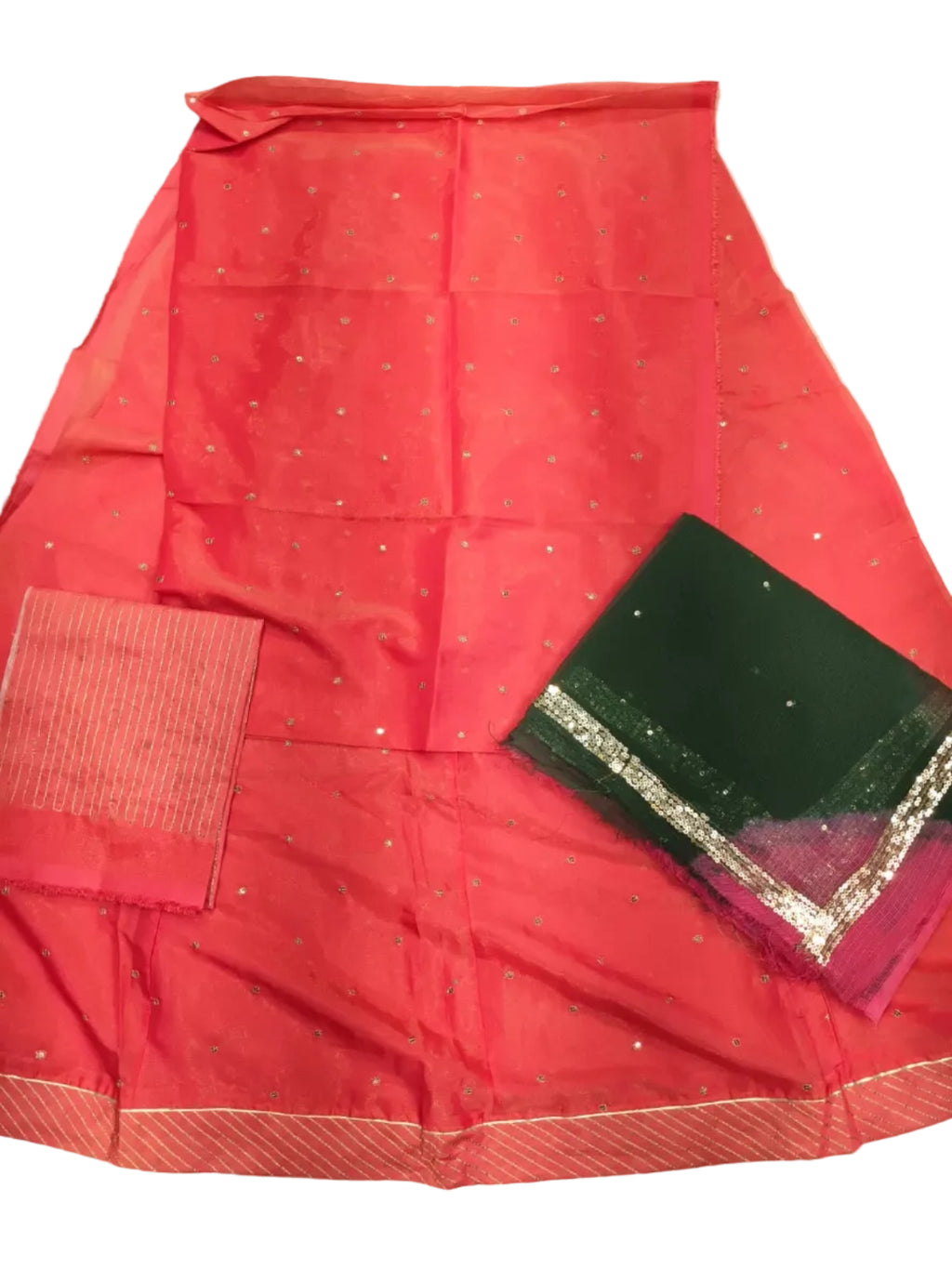 A folded coral pink saree with small silver motifs and a striped border, laid out on a white fabric surface. A dark green fabric piece with metallic silver and magenta borders is placed on top.
