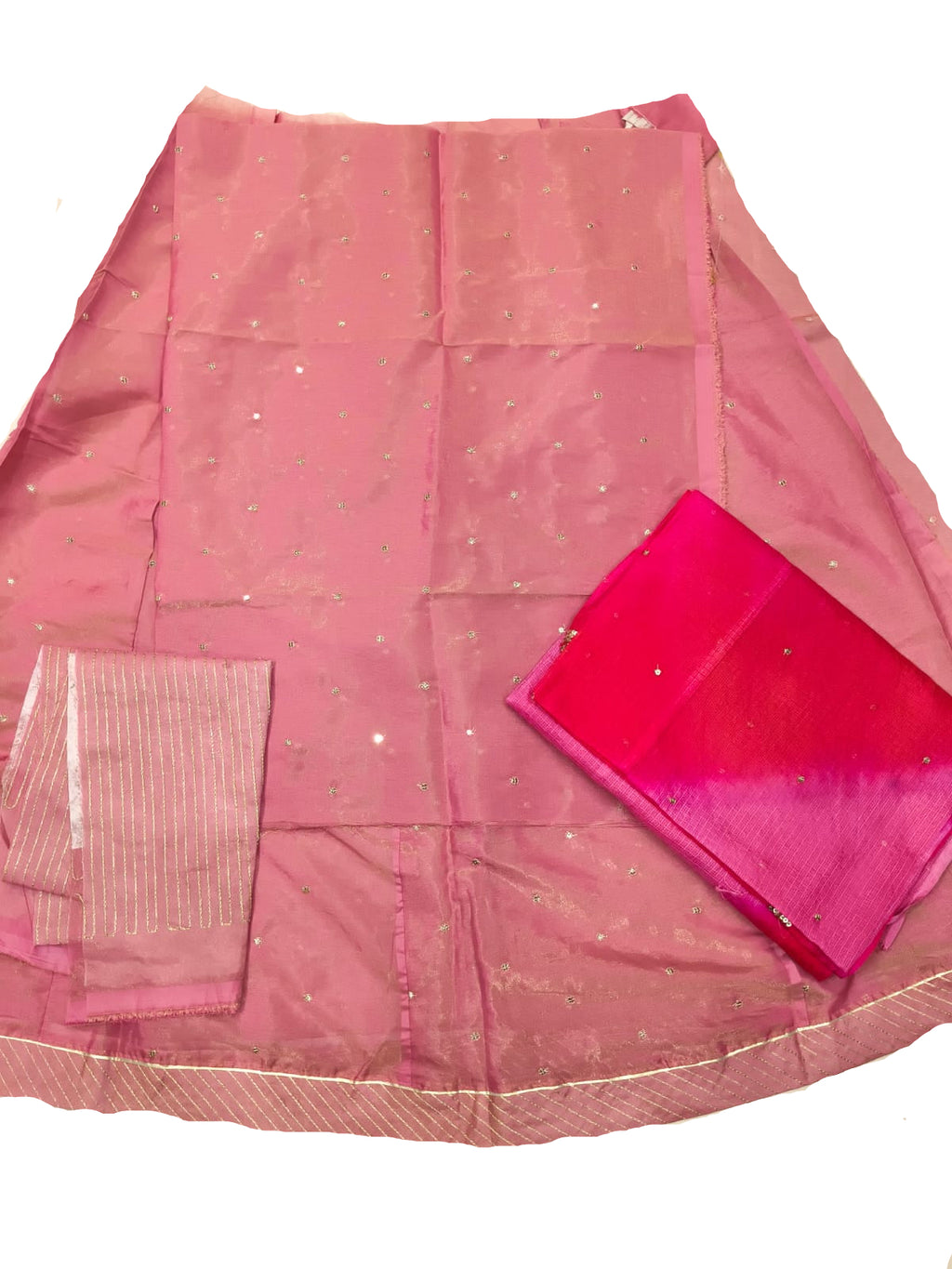 A pink fabric garment laid flat on a light surface, with a matching sheer pink dupatta or scarf featuring small reflective embellishments and a bright pink folded fabric piece placed on top.
