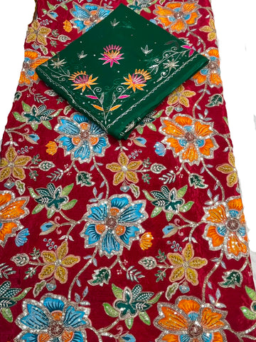A red embroidered fabric with colorful floral patterns in blue, orange, and green, featuring a matching folded dark green embroidered cloth placed on top.