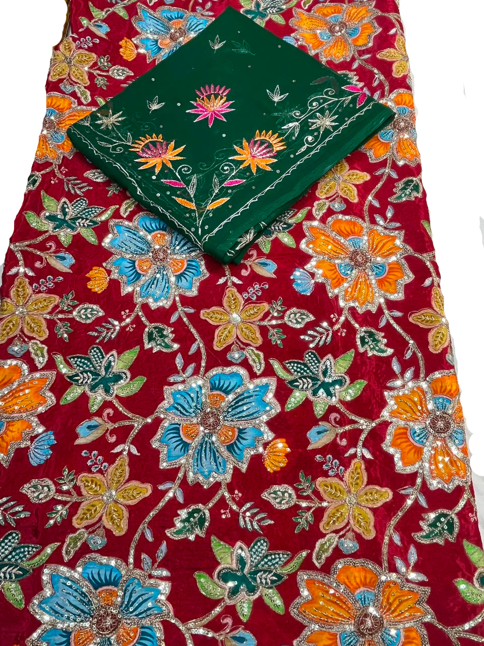 A red embroidered fabric with colorful floral patterns in blue, orange, and green, featuring a matching folded dark green embroidered cloth placed on top.