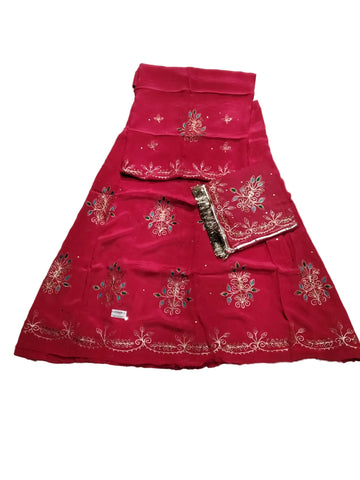 A bright pink traditional skirt set with floral embroidery and a matching dupatta, laid flat on a wrinkled gray sheet.