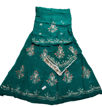 A teal green traditional skirt with intricate silver and orange floral embroidery, laid flat on a wrinkled light gray fabric background.