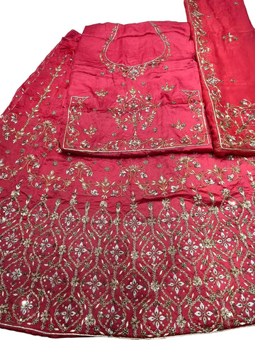 A bright pink traditional embroidered outfit laid flat on a light surface, featuring extensive gold and silver mirror work and floral embroidery across the fabric.