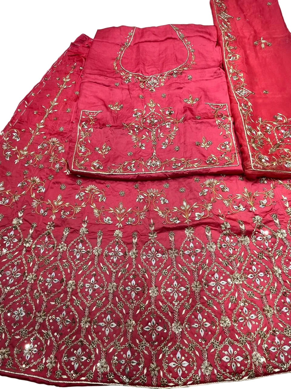 A bright pink traditional embroidered outfit laid flat on a light surface, featuring extensive gold and silver mirror work and floral embroidery across the fabric.