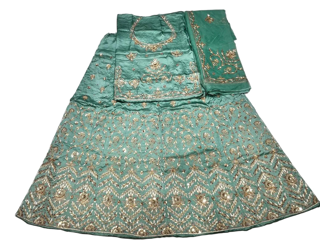 A mint green traditional ethnic garment laid flat on a white fabric background, featuring extensive gold zari embroidery and mirror work.