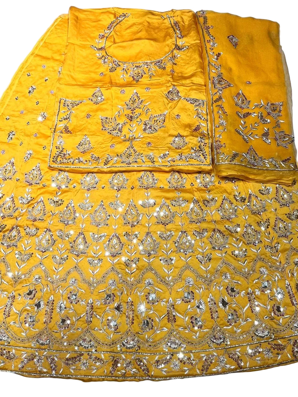 A bright yellow traditional outfit laid flat on a white surface, featuring extensive gold and silver mirror work embroidery across the fabric.