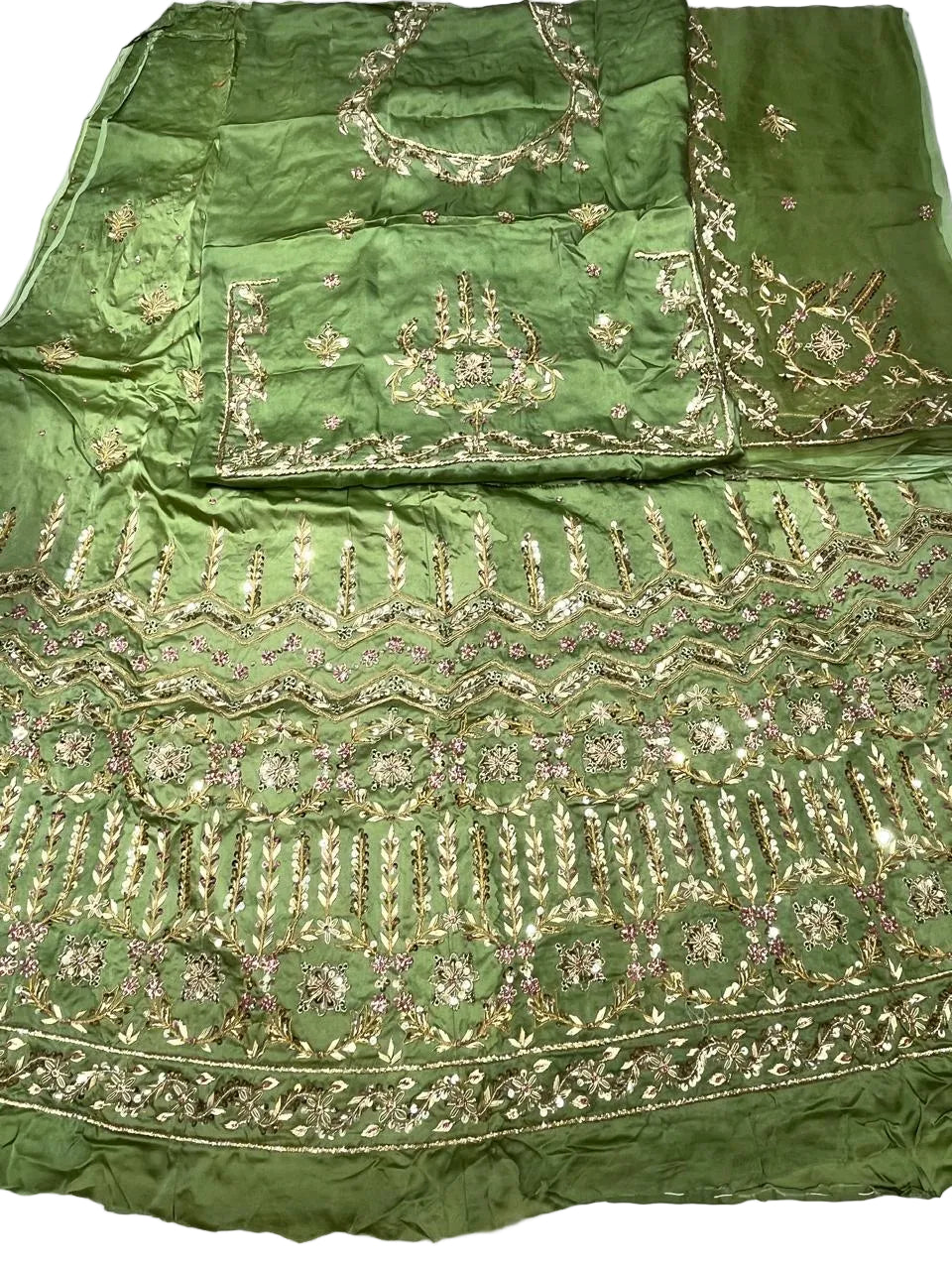 Green embroidered fabric set laid flat on a white surface, featuring ornate metallic gold and pink mirror work embroidery with floral and geometric patterns.