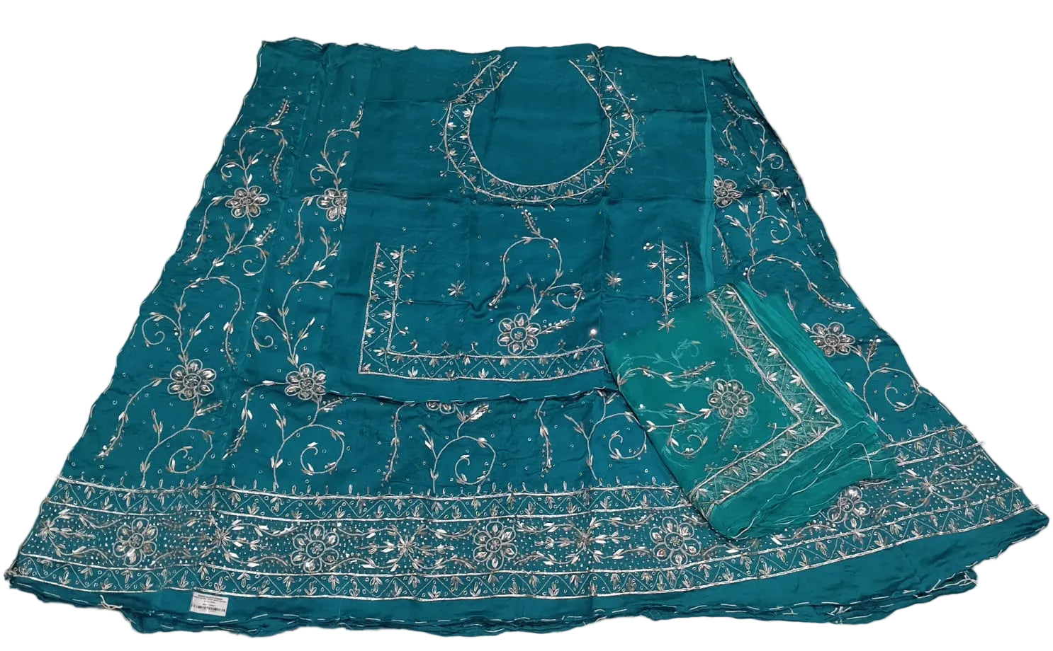 Teal fabric with white embroidery on a beige surface
