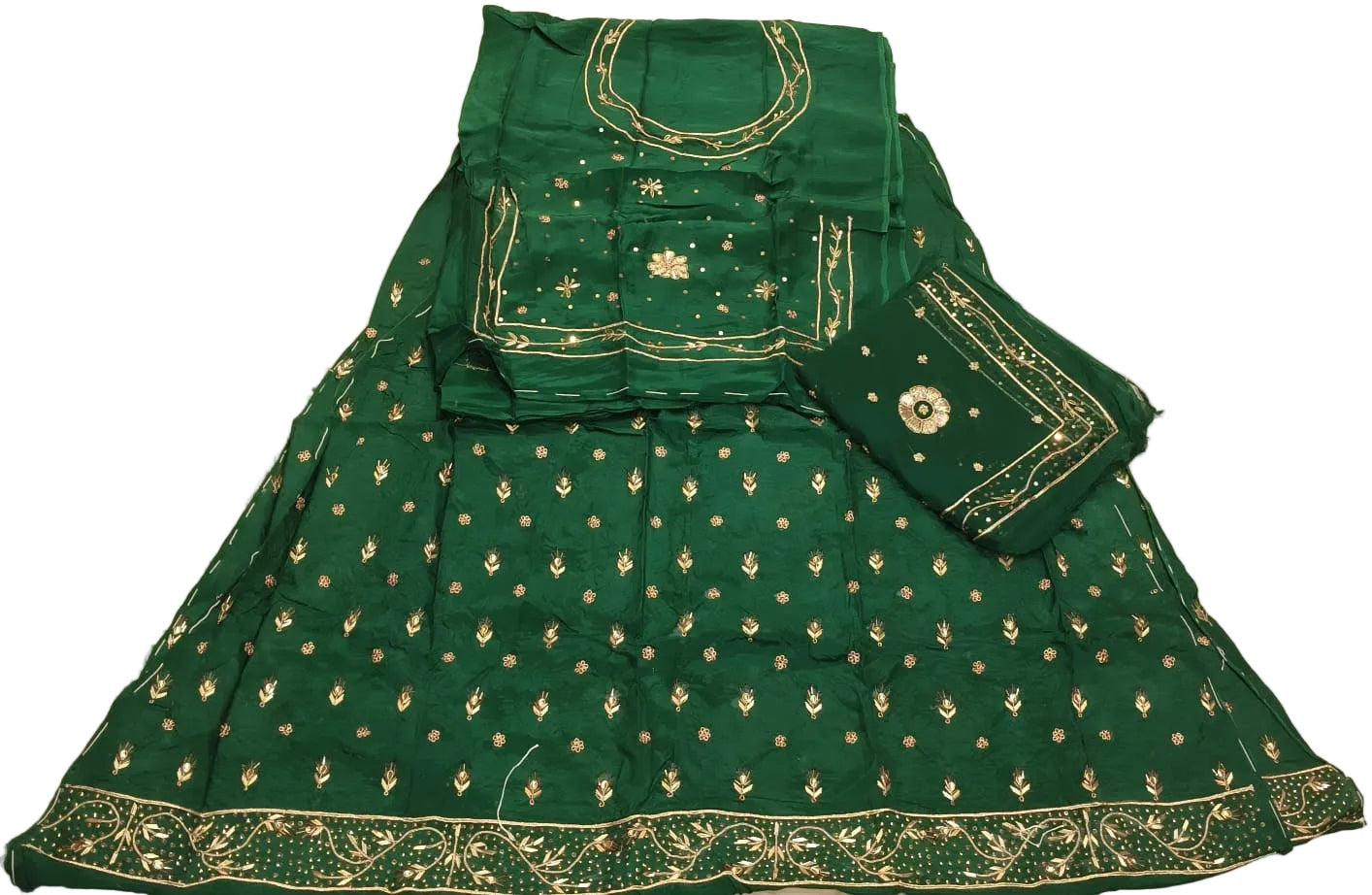 Green traditional outfit with gold embroidery on a white bedspread