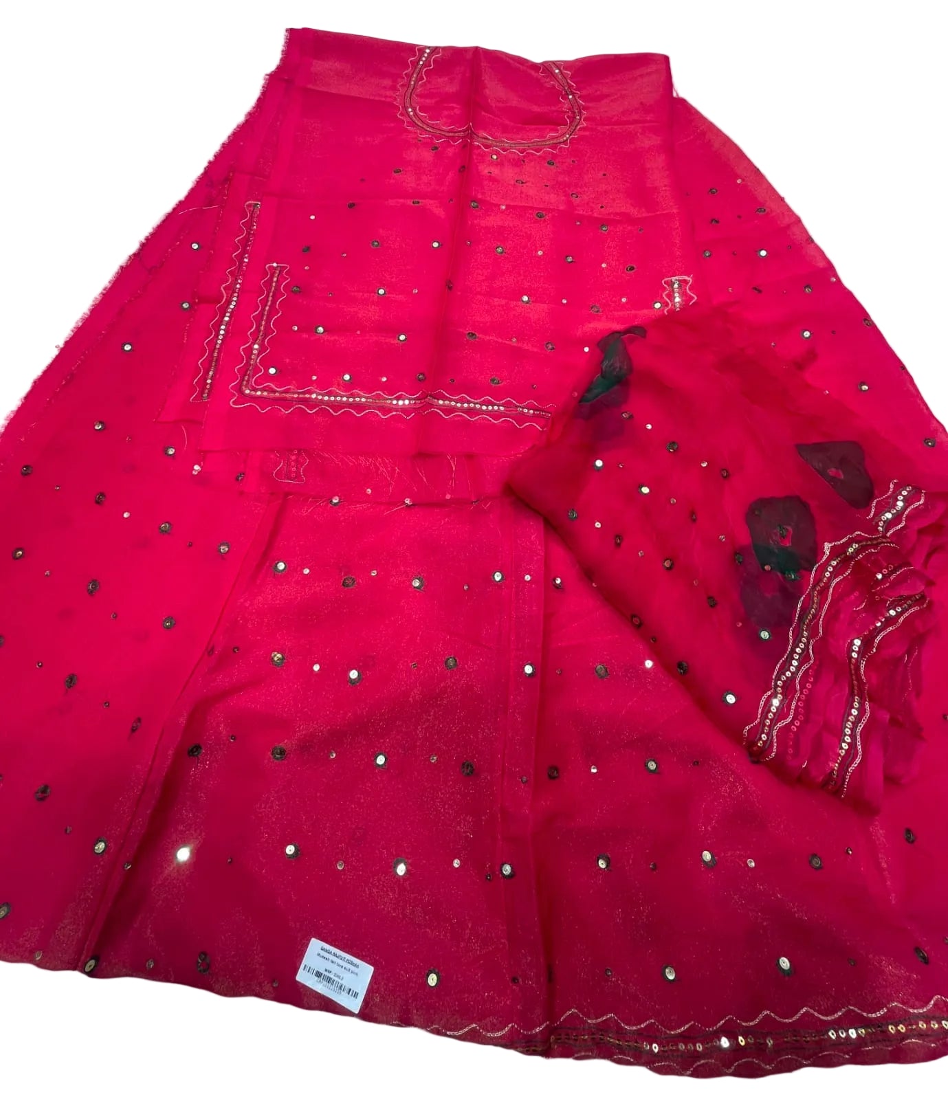 A bright pink traditional skirt set with matching dupatta, featuring silver mirror work embellishments and gold zari embroidery, laid flat on a white fabric background.