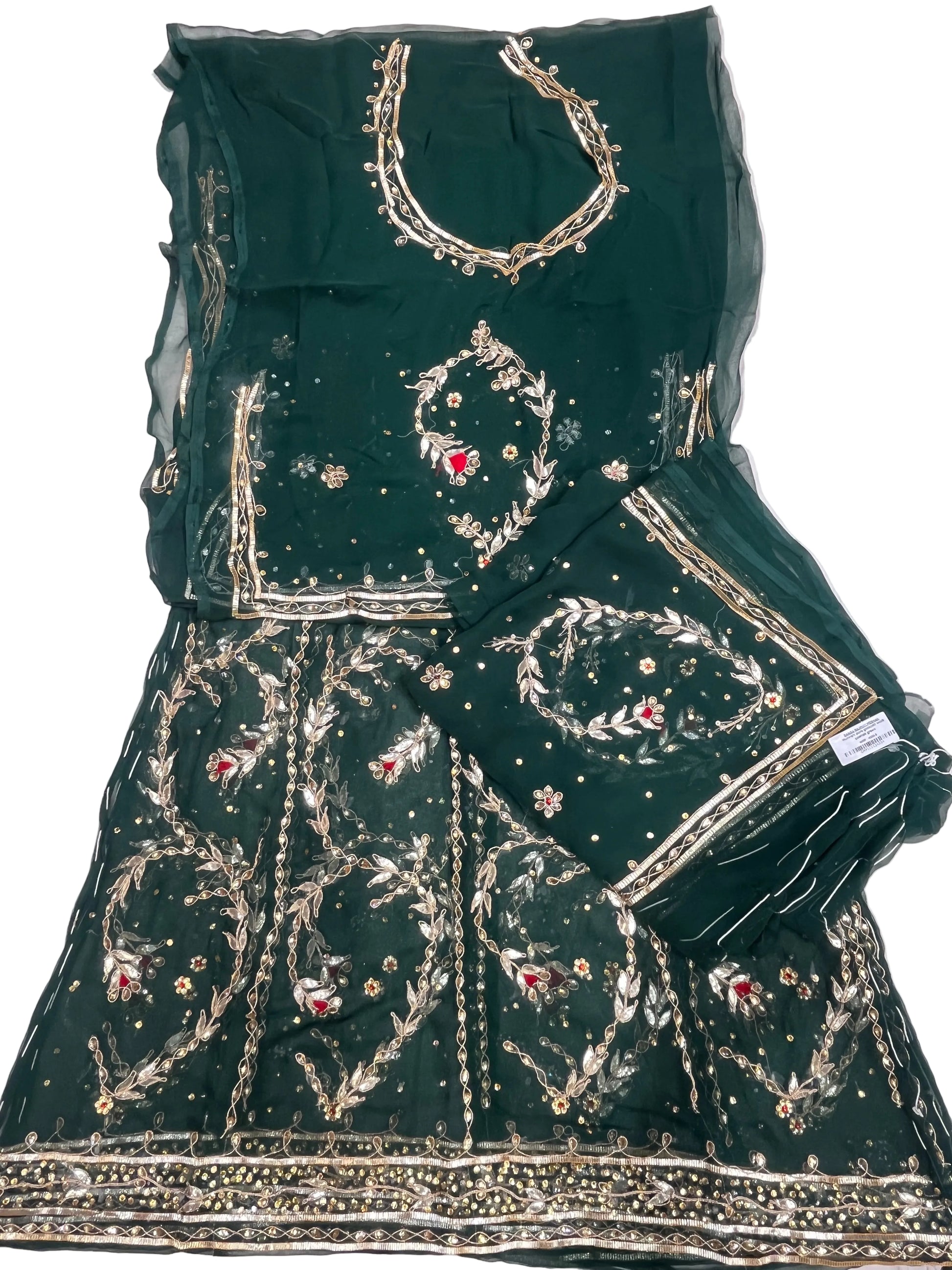A dark green embroidered traditional rajputi outfit laid flat on a white fabric surface, featuring a flared skirt or dupatta piece with extensive gold embroidery, beadwork, and small red floral accents, plus a matching sheer green blouse piece with gold neckline detailing.
