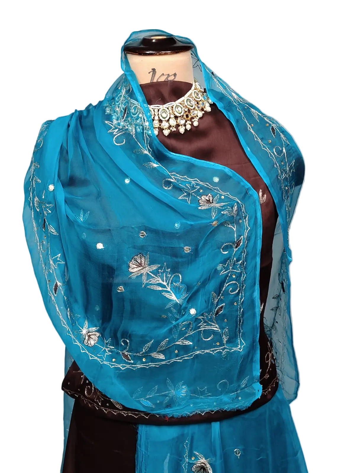 A bright turquoise blue sheer dupatta with silver floral embroidery and mirror work, draped over a dark brown satin blouse on a mannequin torso.