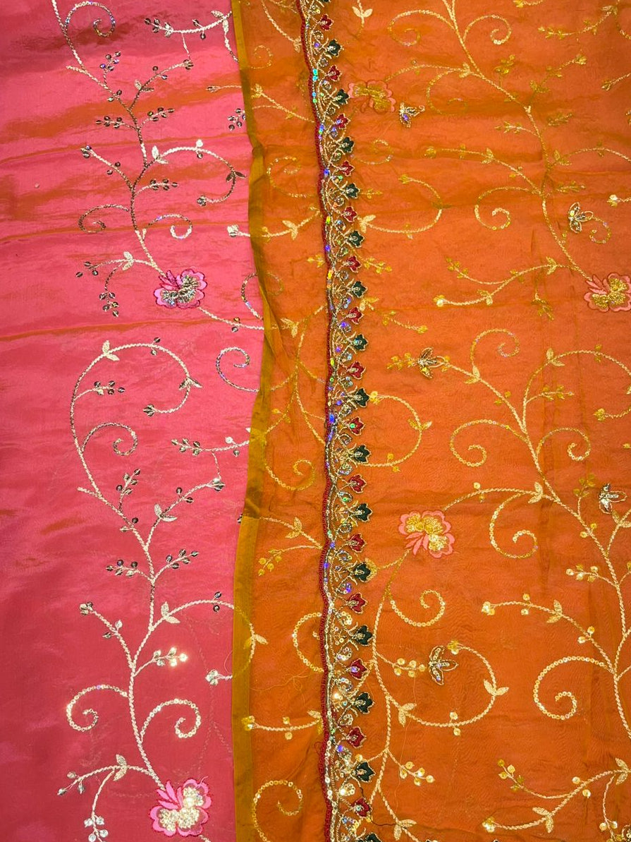 Orange and pink fabric with intricate gold embroidery on a wooden surface